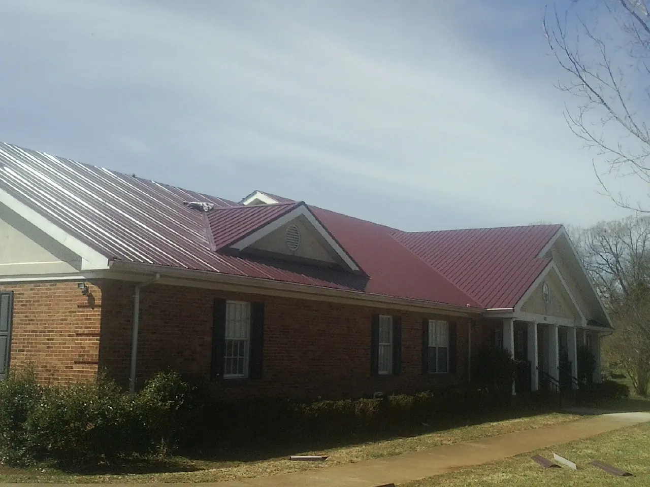 Red metal roof with gabled entries on a long brick building, from a Hail Damage Roof Repair job in Sumas