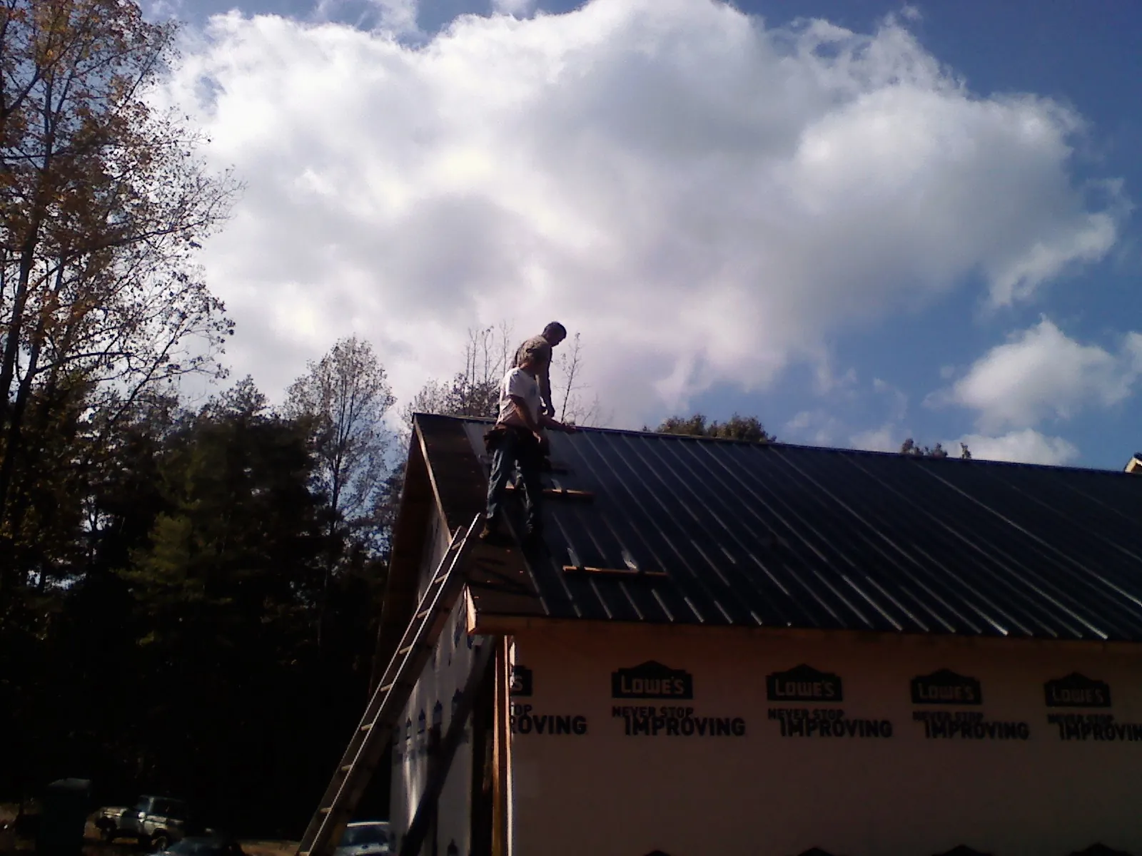 Roofer fastening dark metal panels high against a cloudy sky, from a Roof Inspection job in Sumas